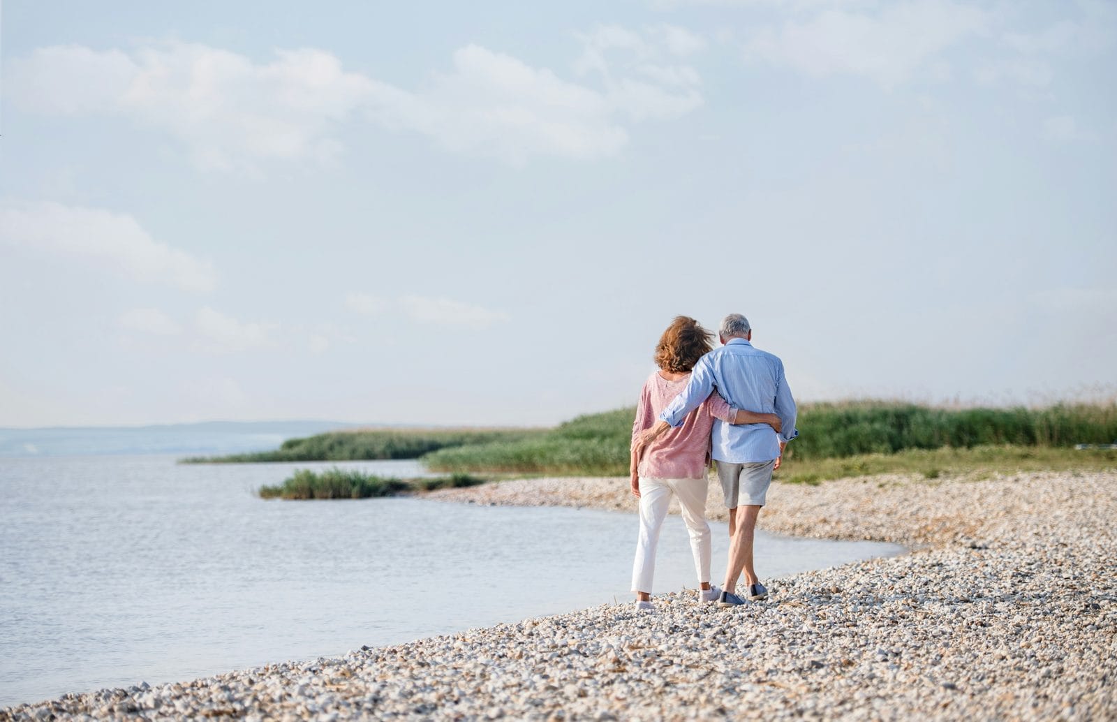A couple walking together along a quiet shoreline, seen from a distance