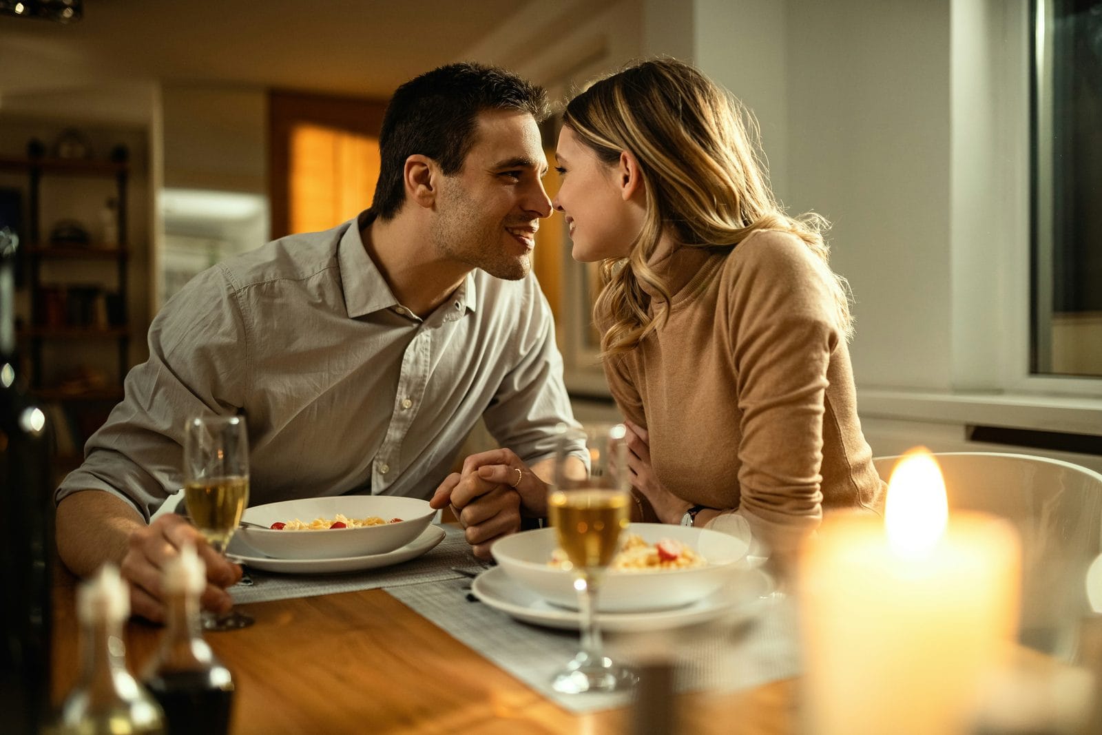 A couple leaning close at a candlelit dinner table