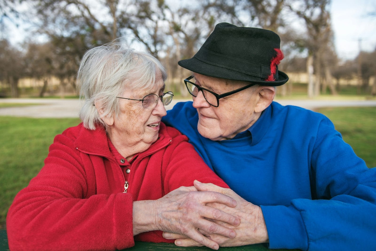 An older couple sitting close together outdoors, holding hands