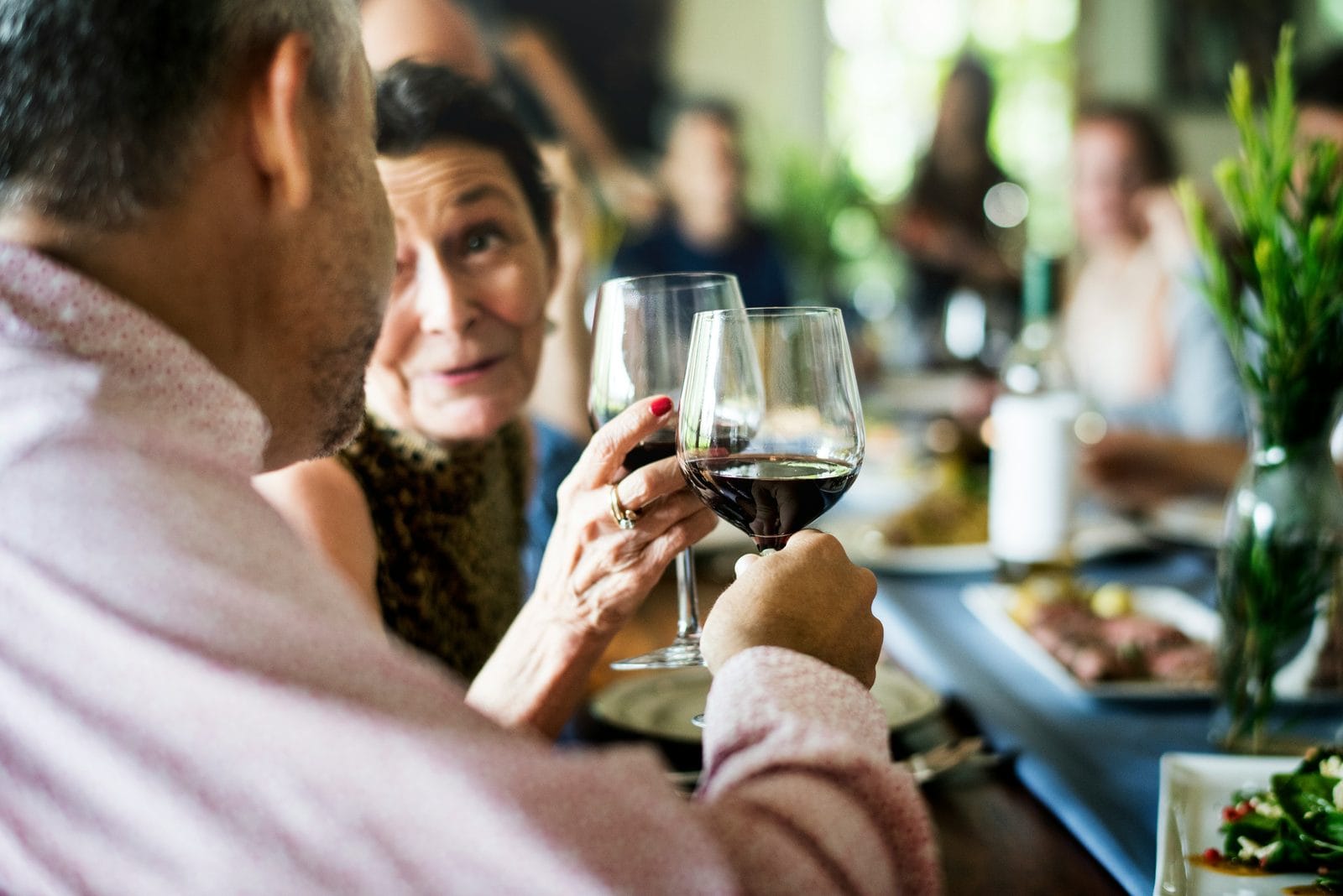 Friends raising glasses of red wine at a busy outdoor dinner table