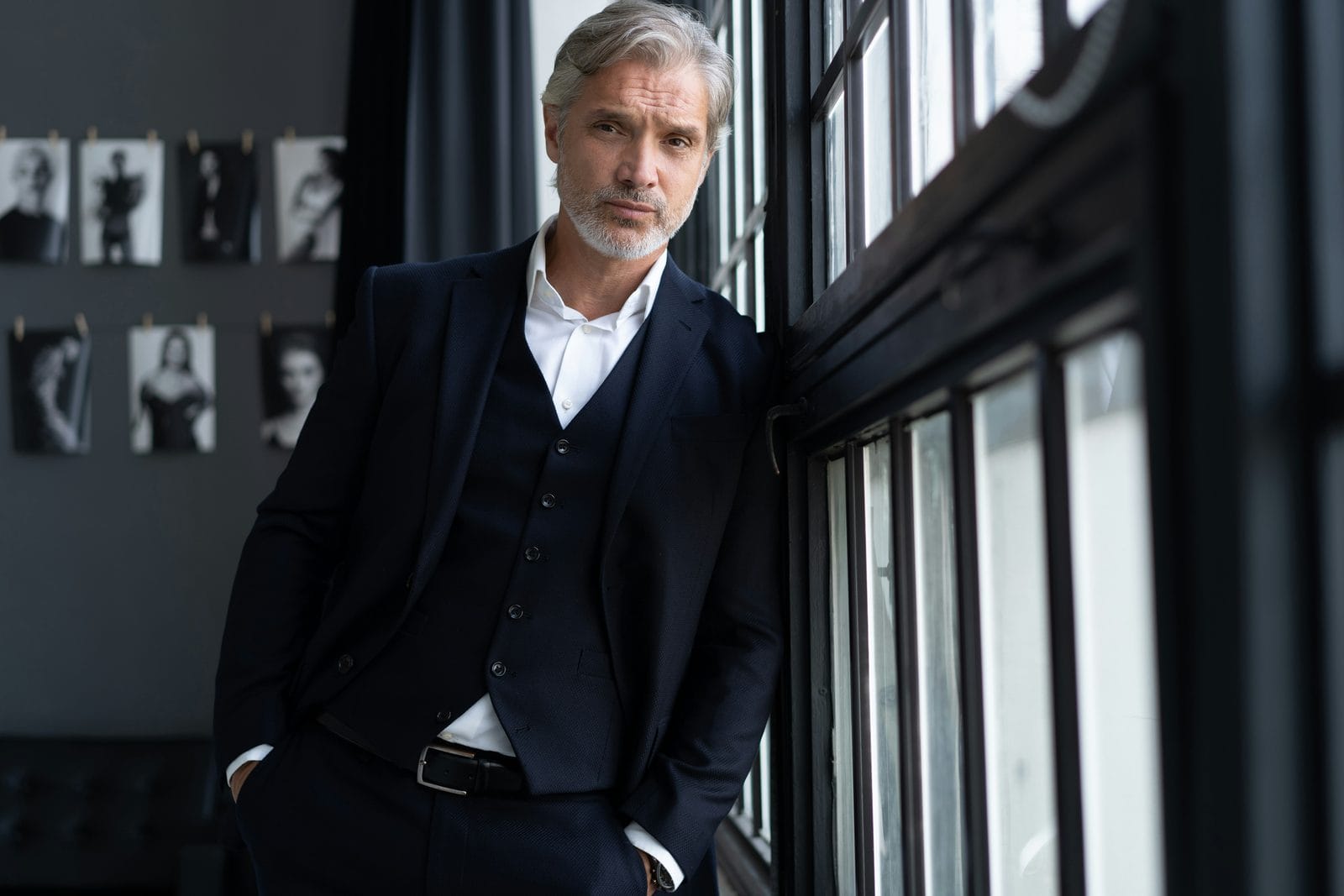 A man in a dark suit standing beside a window