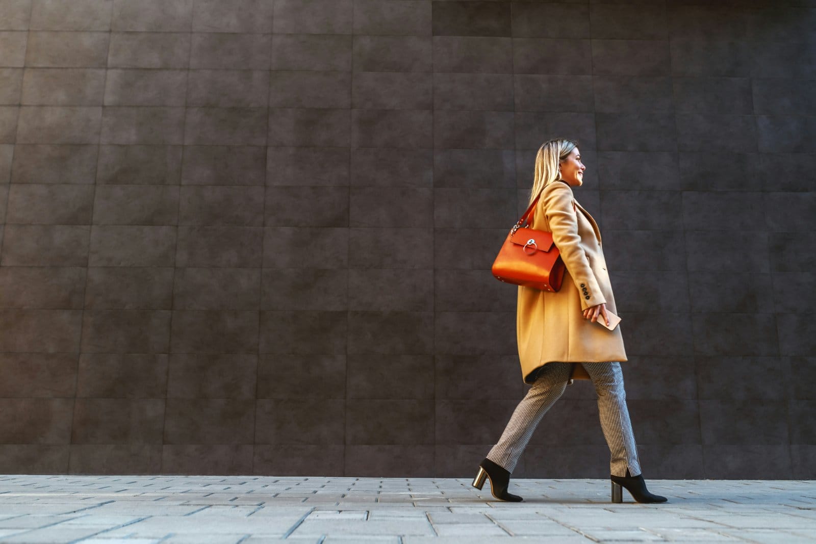 A woman in a coat walking past a grey wall