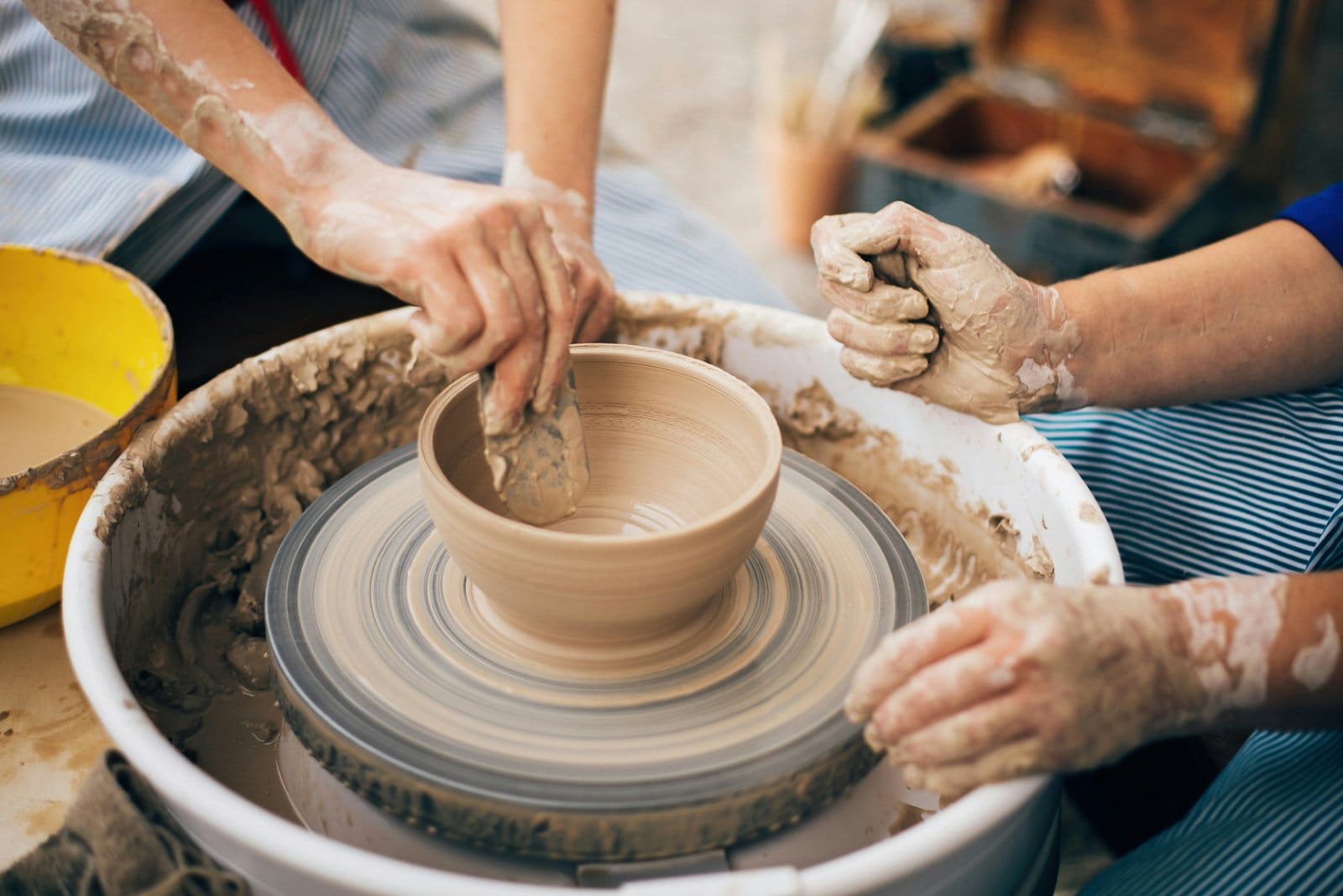 Two people shaping a clay bowl on a pottery wheel