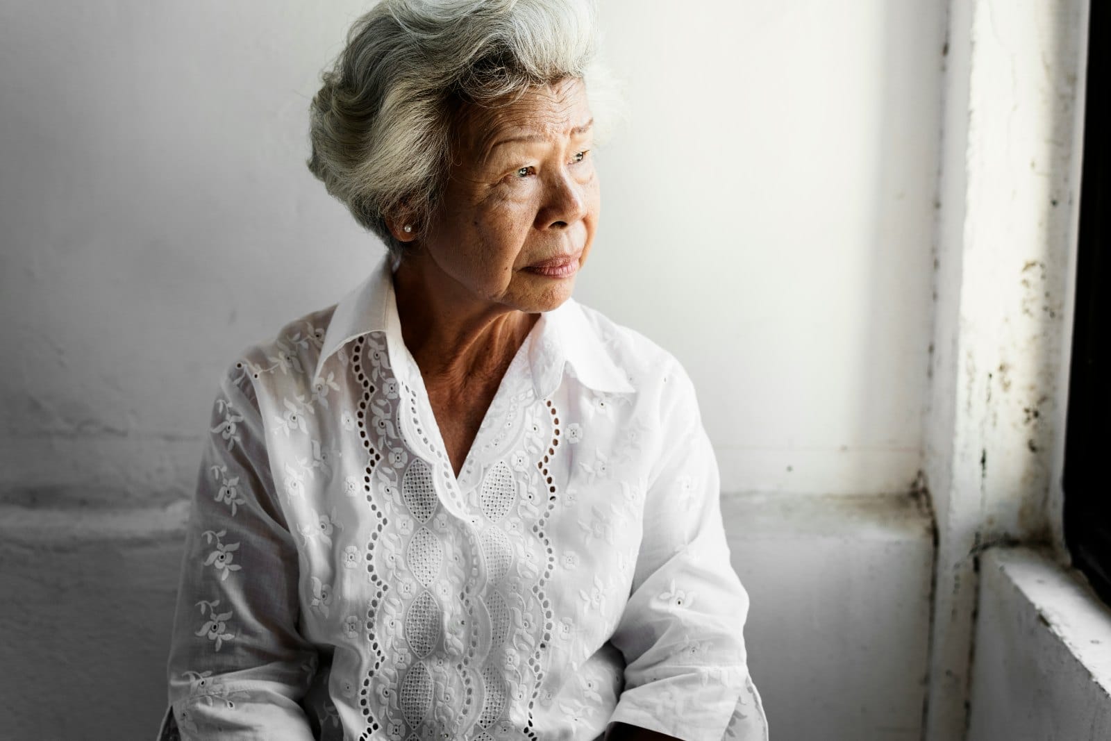 An older woman sitting beside a window, looking out with a thoughtful expression