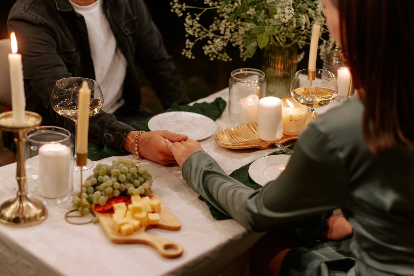 Two people holding hands across a candlelit dinner table