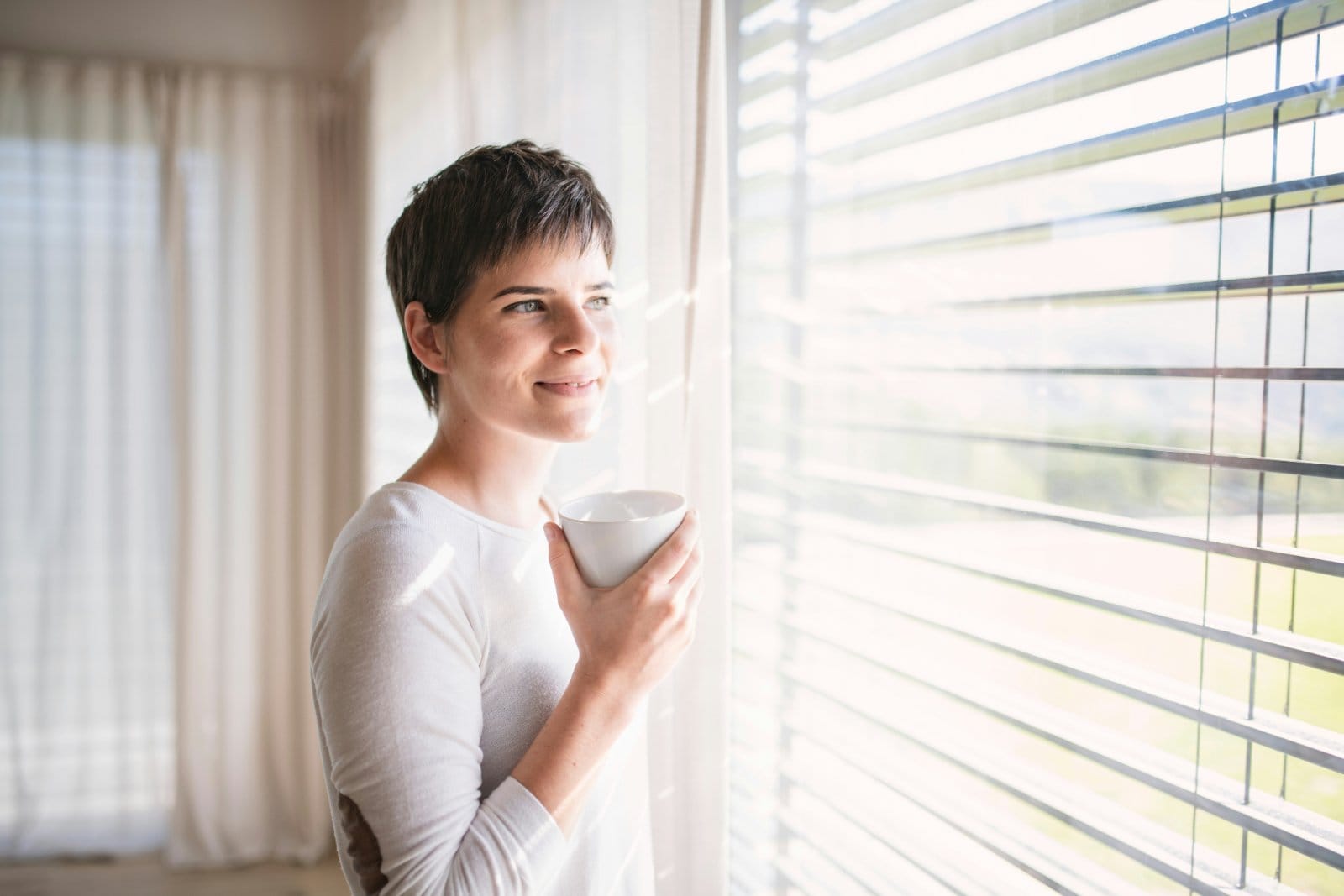 A woman holding a cup of coffee by a window