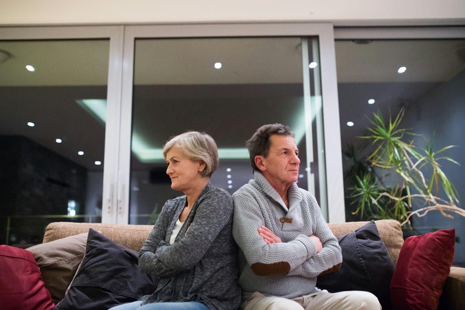 A couple in their sixties sitting at opposite ends of a sofa, both looking away