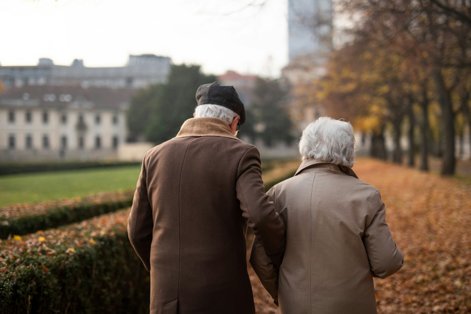 An older couple walking arm in arm along a park path in autumn